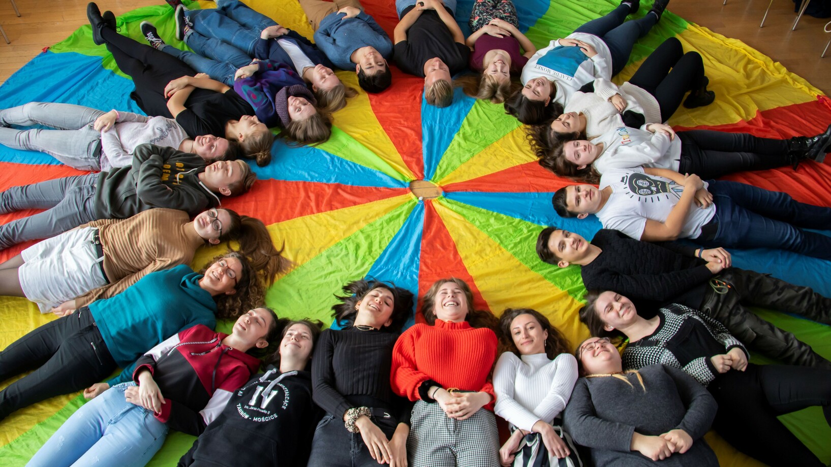 Jugendliche liegen im Kreis auf einem Regenbogen