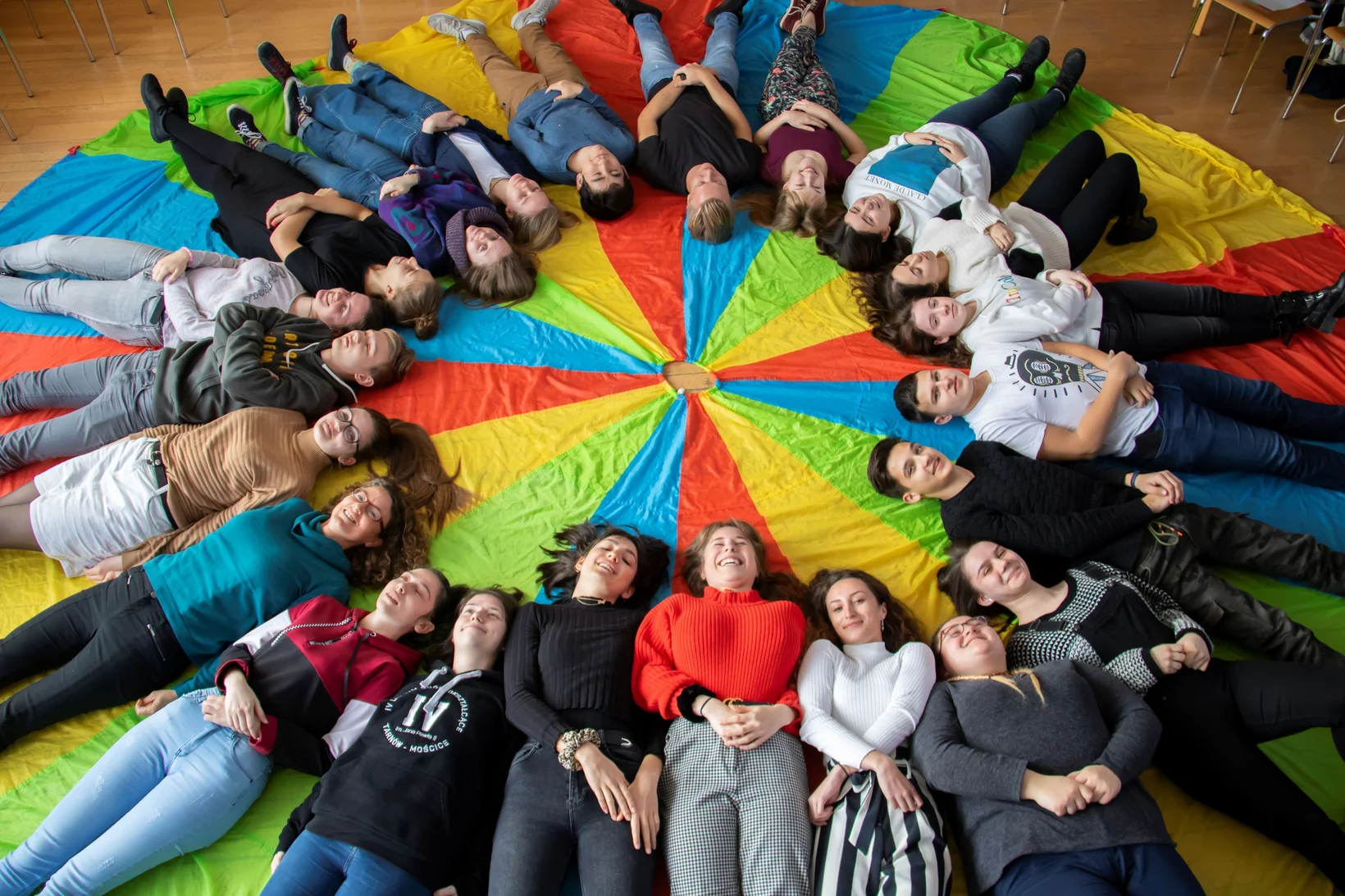 Jugendliche liegen im Kreis auf einem Regenbogen